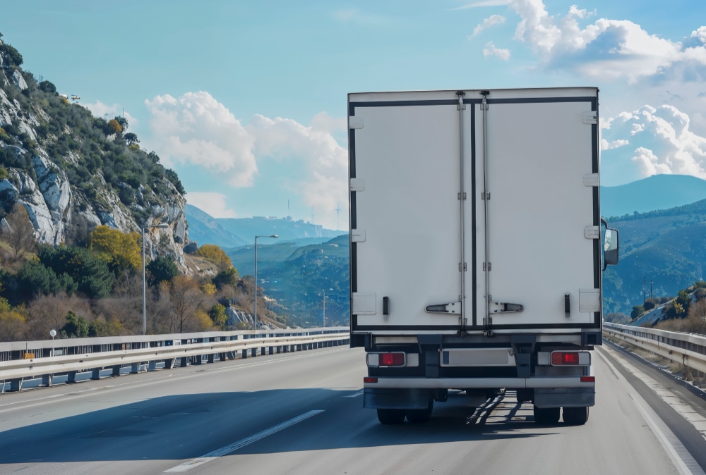 Rear view of a white delivery truck driving through a mountainous highway.