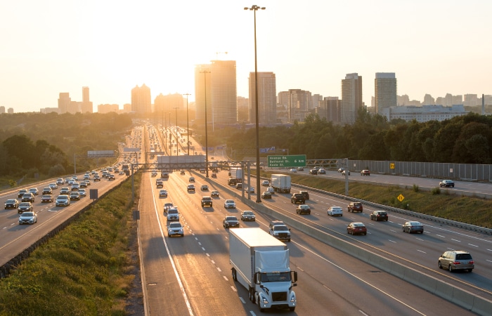 Multiple heavy trucks driving on a U.S. interstate near a city skyline