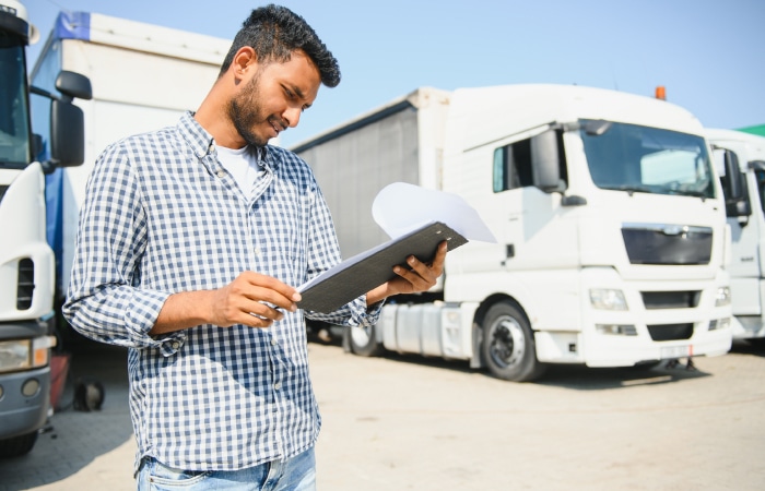 Logistics manager reviewing route plans in front of HGV trucks.