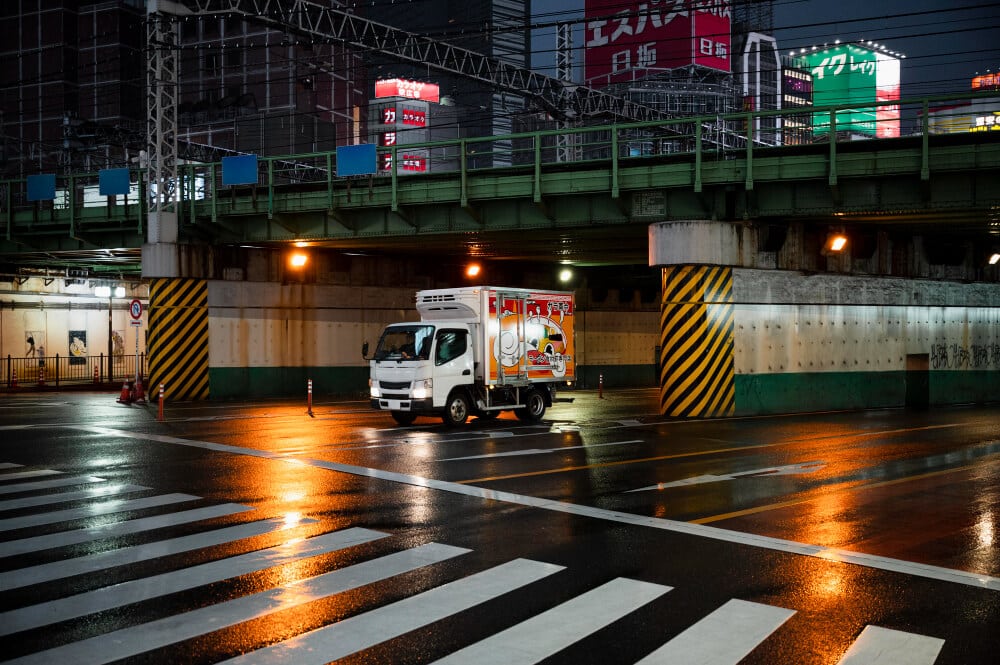 Delivery truck driving through a city underpass at night.
