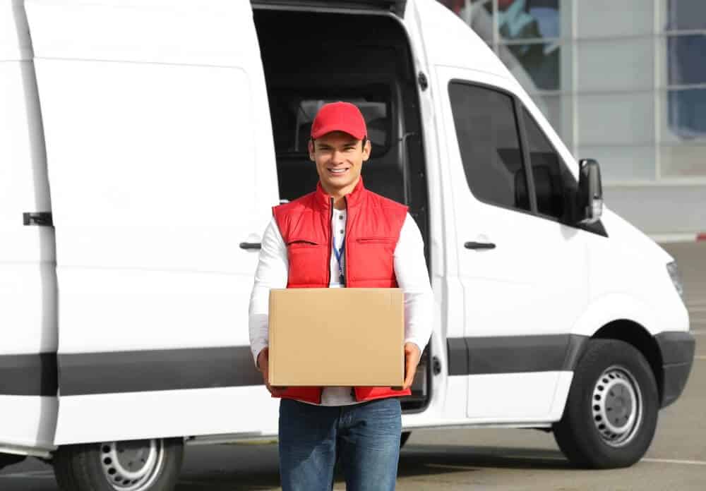 Smiling courier with parcel in front of a fully loaded delivery van