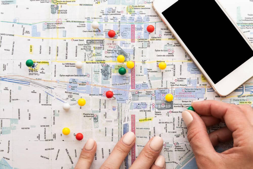 Hands placing pins on a paper map beside a smartphone.